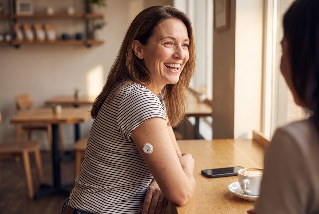 Mujer riendo en un café con el celular boca abajo sobre la mesa y el sensor QiTrax en el brazo